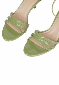 Sandali con tacco alto in pelle verniciata verde, con più cinturini stretti e punta affusolata, dotati di una soletta beige e un tacco piccolo.