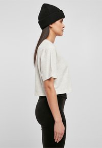 Camiseta gris recortada de manga corta, combinada con pantalones negros de cintura alta. La modelo lleva un gorro de punto negro. Vista de perfil lateral.
