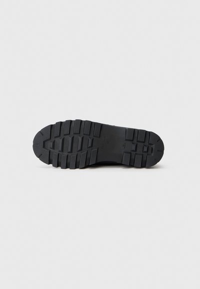 Black rubber outsole with textured tread pattern, featuring deep grooves and a flat heel for traction and stability.