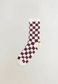 Witte sok met een bordeauxrood en wit geblokt patroon plat gelegd op een lichte neutrale achtergrond.