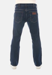 Jeans de mezclilla azul oscuro con un ajuste de pierna recta, bolsillos traseros visibles con un diseño en zigzag y una etiqueta de cuero marrón en la cintura.