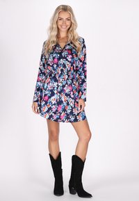 Rochie bleumarin cu maneci lungi și talie strânsă, având flori roz aprins, albe și albastre. Asortată cu cizme cowboy din suede negre.