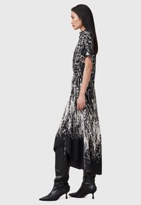 Vestido hasta la rodilla en un patrón abstracto en blanco y negro, hecho de un tejido suave. Presenta mangas cortas y una silueta fluida, acompañado de botas negras.