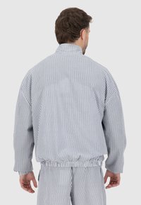 Veste rayée en bleu clair et blanc, avec un col montant, une taille élastique et une coupe ample. Tissu texturé avec des épaules tombantes.