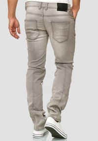 Šedé džíny z denimu s přiléhavým střihem, pěti kapsami, mírným opotřebením a černou koženou záplatou na pasu, doplněné bílými teniskami.