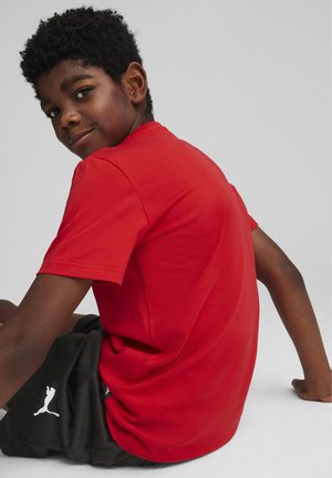 Camiseta de algodón roja con mangas cortas, cuello redondo y textura suave. Combinada con pantalones cortos negros que tienen un logo blanco cerca del dobladillo.