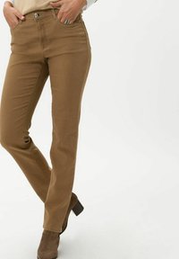 Jeans rectos marrones con una textura suave, cierre de botón metálico y diseño de cinco bolsillos, combinados con botas de tacón marrones.