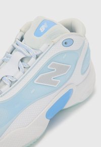 Ljusblå sportskor med nät- och syntetmaterial, med en strukturerad vit sula och silverfärgad logotypdetalj på sidan.