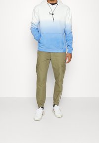 Biała i niebieska gradientowa bluza z kapturem, kangurza kieszeń, zestawiona z oliwkowymi spodniami cargo z bocznymi kieszeniami i elastycznymi mankietami.