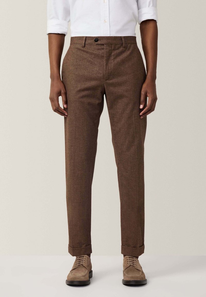 Braune, strukturierte Hose in Slim-Fit-Form mit einem Knopfverschluss und umgeschlagenen Säumen. Kombiniert mit hellen Schuhen.