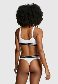 Weißer Sport-BH und String mit schwarzem "PUMA"-Gummibund. Glattes Material, verstellbare Träger, Rückenpartie, die Komfort und Passform betont.