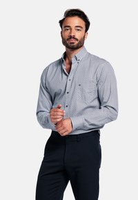 Wit en marineblauwe geometrische patroon knoopshirt; lange mouwen; enkele borstzak; gecombineerd met donkere broek.