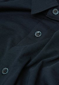 Mörkblå skjorta med texturerad tyg, klassisk krage och två knappar med en lätt lyster.