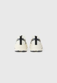 White sneakers with a textured upper, black accents, and a thick sole. Features a pull tab and "ONE" branding on the heel.