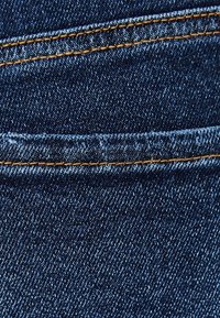 Tela de mezclilla azul oscuro con una textura suave, que presenta costuras amarillas a lo largo de las costuras, resaltando los detalles de diseño de la prenda.