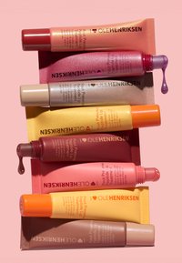 Sieben Tuben Ole Henriksen Pout Preserve Peptide Lip Treatment in verschiedenen Farben, zwei mit Produkt, das von den offenen Kappen tropft.