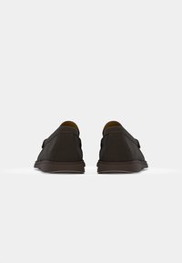 Chaussures en daim marron avec une texture lisse, une forme arrondie et des semelles en caoutchouc marron ; présentant un design minimaliste et sans matériel visible.