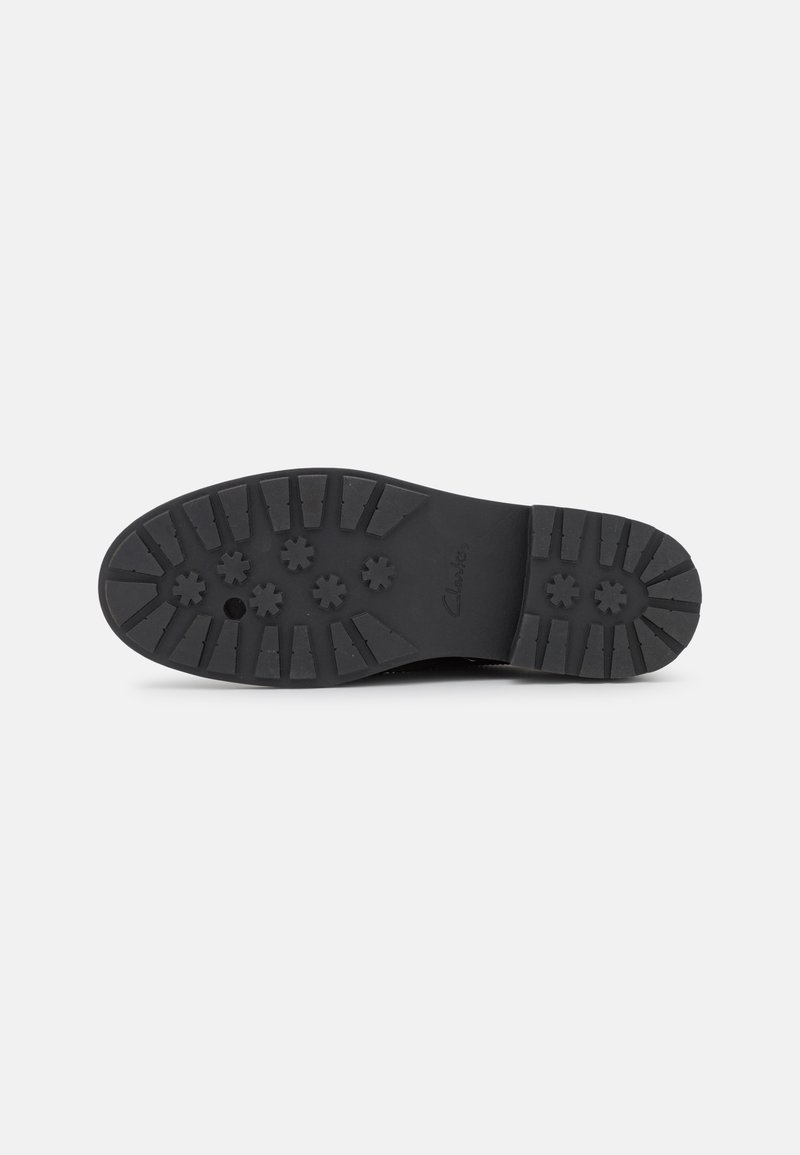 Semelle de chaussure en caoutchouc noir avec un motif texturé comportant plusieurs motifs en forme d'étoile et des rainures pour l'adhérence, étiquetée "Clarks."