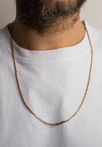 Guldkæde med ovale led, båret over en hvid t-shirt. Glat tekstur, medium tykkelse, hænger løst omkring halsen.