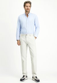 Camicia azzurro chiaro con bottoni, pantaloni bianchi e sneakers grigio-neri. La camicia ha un tessuto texturizzato, mentre i pantaloni sono lisci con un design aderente.