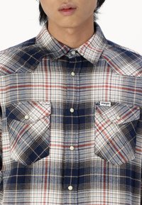 Chemise à carreaux dans des nuances de bleu, crème et rouge. Dotée d'un col étalé, de deux poches poitrine et de boutons. Fabriquée en tissu texturé.