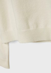 Hellcremefarbener Pullover mit weicher Textur und geripptem Saum. Das Design umfasst einen hinten etwas längeren Schnitt im Vergleich zur Vorderseite.