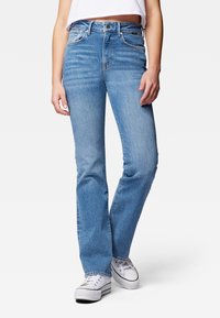 Jeans de mezclilla de tiro alto, de corte acampanado y color azul claro, con bolsillos delanteros y costuras blancas. Combinados con zapatillas blancas.