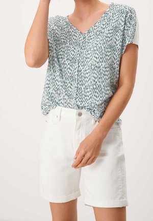 Kortærmet top i lyseblå med et spredt sort og teal mønster, kombineret med hvide, optrukne denimshorts. Afslappet og løstsiddende pasform.