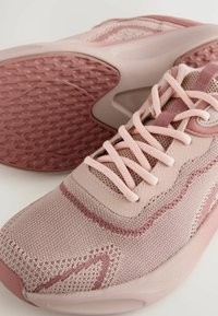 Baskets de sport rose clair avec une tige en mesh texturé, dotées de lacets et d'une semelle en caoutchouc à motif pour une adhérence et un soutien.