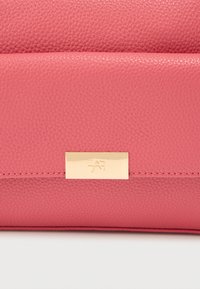 Ροζ δερμάτινο πορτοφόλι με υφή, διακοσμημένο με πλάκα από χρυσό μέταλλο με ανάγλυφο λογότυπο. Ραφή στην άκρη.