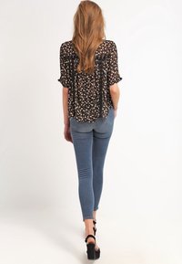 Blouse noire à motifs avec manches courtes à volants, associée à un jean skinny bleu. Détails remarquables : une coupe ample et fluide ainsi qu'une texture contrastante.