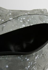 Bolsa de tela verde con un patrón moteado, cierre con cremallera y interior negro. Material resistente con textura suave y costuras reforzadas.