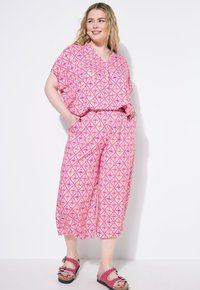 Roze gestreepte jumpsuit met een V-hals, korte mouwen en wijde broekspijpen. Beschikt over een geometrisch ontwerp met zakken en gecombineerd met roze sandalen.