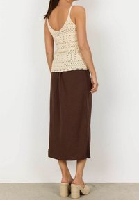 Lichtbeige, aansluitend gehaakt topje met dunne bandjes en geperforeerde details, gecombineerd met een vloeiende bruine rok tot de enkels. Gelaagde platte sandalen.