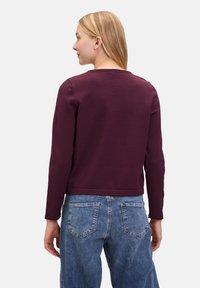 Pull à col rond bordeaux avec manches longues, en tissu texturé, taille courte, associé à un jean en denim bleu clair taille haute.