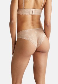 Krajkový spodní prádlo v tělové barvě, s propracovanými květinovými vzory, nastavitelnými ramínky a jemnými texturami. Zadní pohled ukazuje detailní krajkový lem.