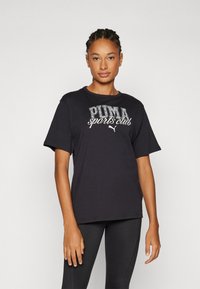 Musta puuvillainen t-paita, jossa on valkoiset tekstit "PUMA sports club". Lyhyet hihat ja pyöreä kaula-auko; rento istuvuus ja minimaalinen rakenne.