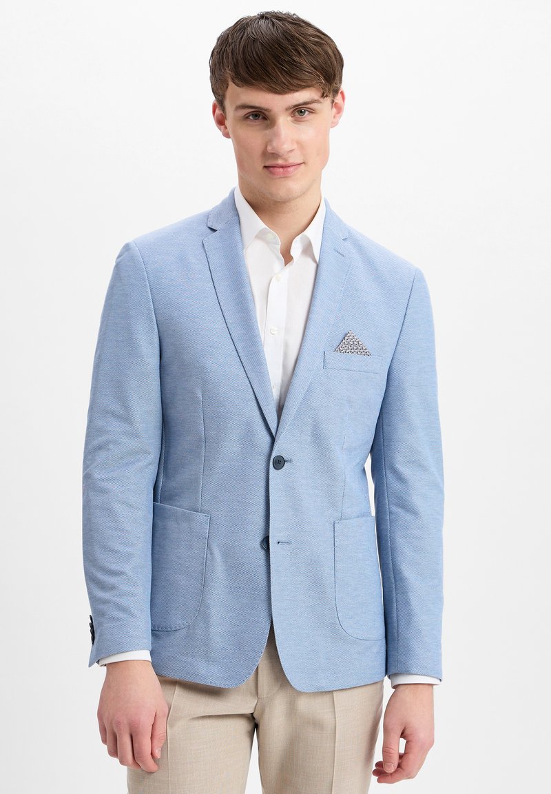 Lichtblauwe blazer met een gestructureerde afwerking, twee voorkanten zakken, enkele knoopsluiting en een stijlvolle pochet. Gestoefd over een wit shirt.