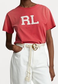 Röd bomulls-t-shirt med vit "RL" logotyp, korta ärmar. Matchad med vita denimbyxor och ett knutet repbälte med metallaccenter.