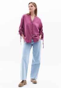 Camicia button-up svasata color malva con maniche lunghe arricciate ai polsini. Abbinata a jeans azzurri e mocassini marroni.