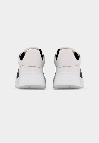 Ζευγάρι λευκών και μαύρων αθλητικών παπουτσιών, εμφανιζόμενα από πίσω πάνω σε απλό ανοιχτό γκρι φόντο.