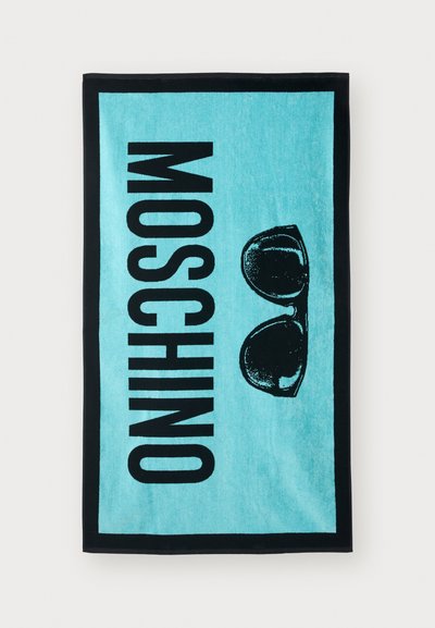 Turquoise beach towel featuring a black border, bold text reading "MOSCHINO," and black sunglasses graphic printed centrally.