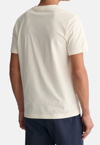 Krémové bavlněné tričko s krátkými rukávy a kulatým výstřihem, s hladkou texturou a minimálním prošitím na zadní straně.