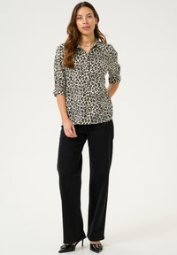 Chemise à motifs léopard avec manches retroussées, associée à un pantalon droit noir et des escarpins noirs à bouts pointus. Texture de tissu lisse.