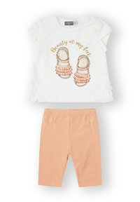 Camisa blanca de manga corta con un gráfico de sandalias y el texto "Belleza a mis pies"; leggings melocotón con cintura elástica y un pequeño acento de corazón.