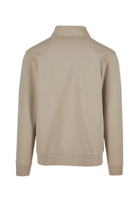 Beige langermet polo skjorte laget av myk stoff, med krage, sømløst skulderdesign og ribbestrikkede mansjett og kant.