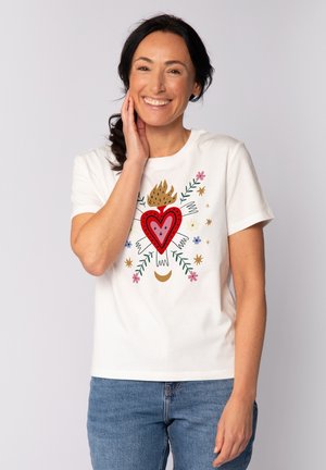 T-shirt en coton blanc avec un graphisme de cœur rouge agrémenté d'accents floraux, de flammes et de motifs d'étoiles colorées. Coupe décontractée avec des manches courtes.