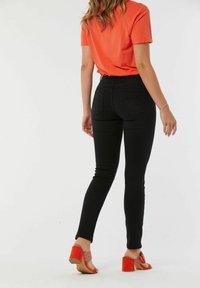Jean skinny noirs à taille haute, avec des poches arrière. Associés à un t-shirt orange et des sandales à talons rouges avec des accents tissés.