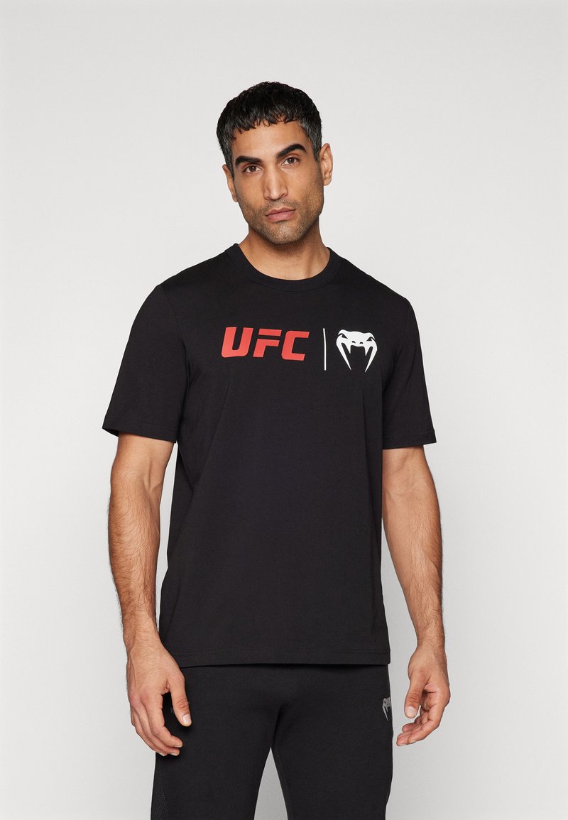 Sorte bomulds t-shirt med et rødt "UFC" logo og et hvidt slangeemblem trykt på brystet. Korte ærmer og rund halsudskæring.