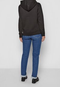 Felpa nera con cappuccio regolabile, abbinata a jeans in denim blu. I jeans sono risvoltati sui polsini e presentano tasche posteriori.